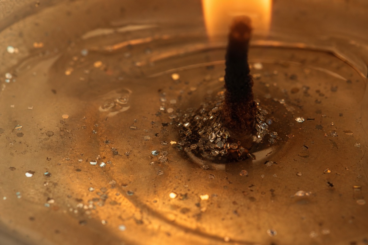 Macro de cire fondue transparente près de la mèche d'une bougie allumée, dans laquelle de minuscules paillettes argentées coulent vers le fond.