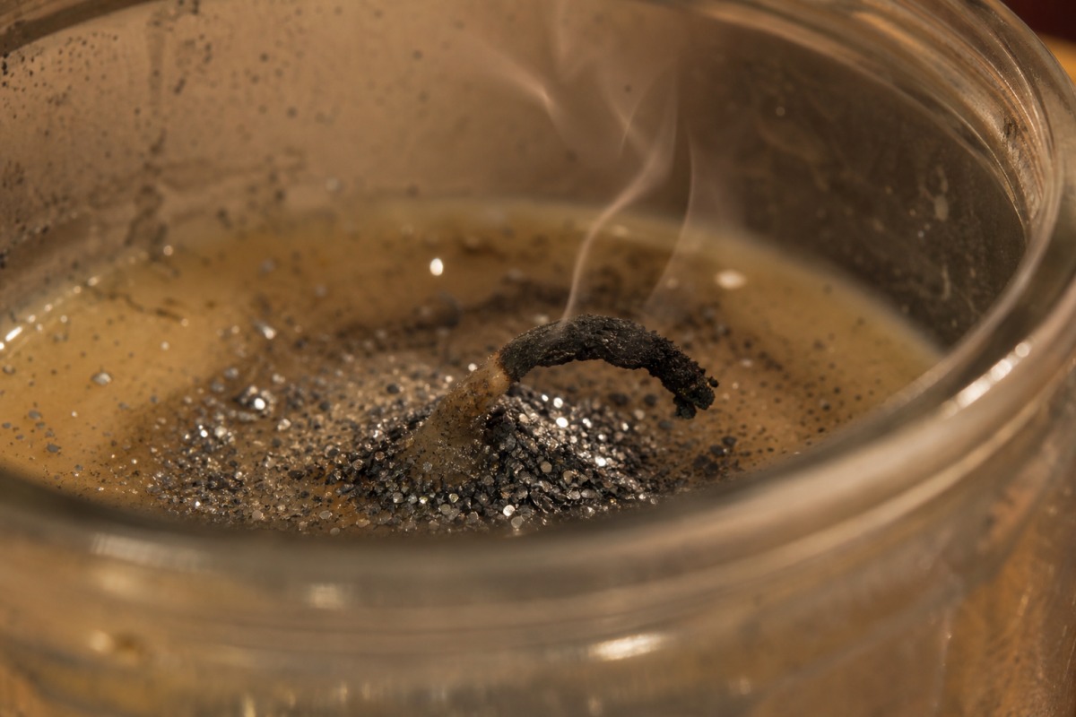 Mèche carbonisée et pliée, recouverte de paillettes argentées accumulées dans la cire figée, la bougie est éteinte.